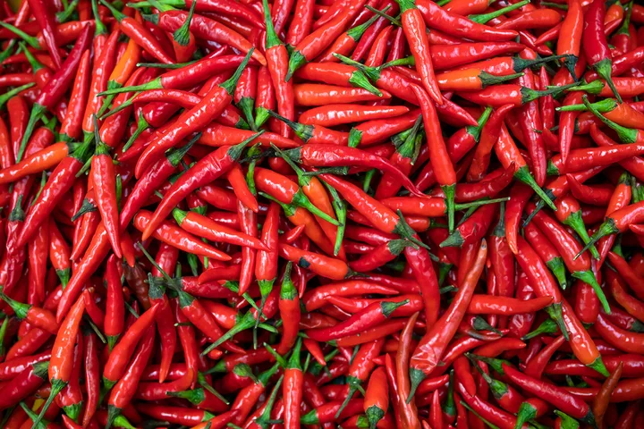 Large pile of vibrant red chili peppers with green stems filling the entire frame.