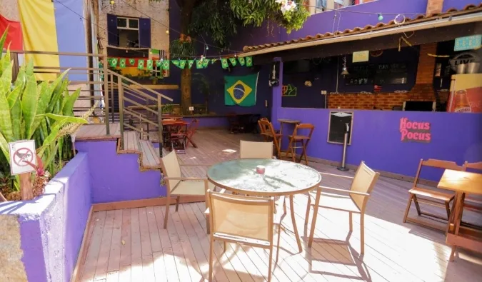Colorful outdoor patio of a hostel with Brazilian flag decor, purple walls, and seating area.