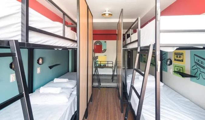 Modern hostel dormitory with metal bunk beds, privacy dividers, and retro wall art.