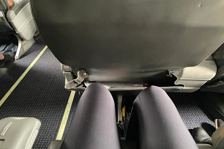 Close-up of a passenger's legs in a cramped economy airplane seat with limited legroom.