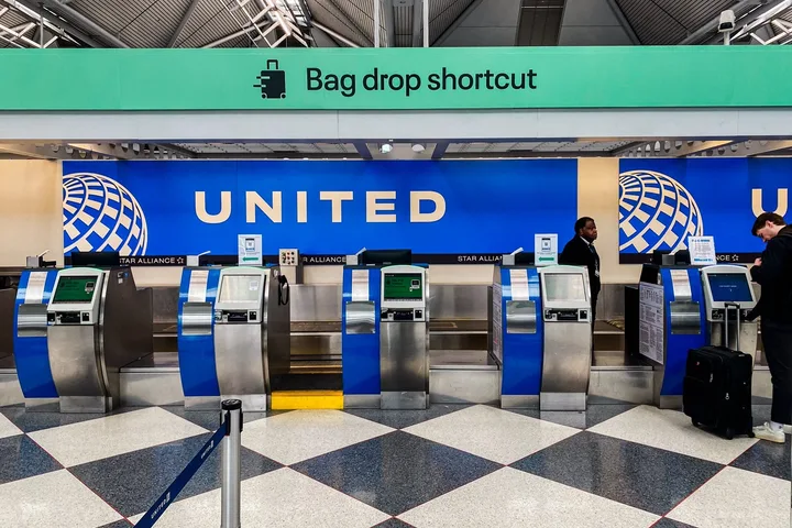 United Airlines self-service bag drop kiosks at an airport terminal with a few travelers.