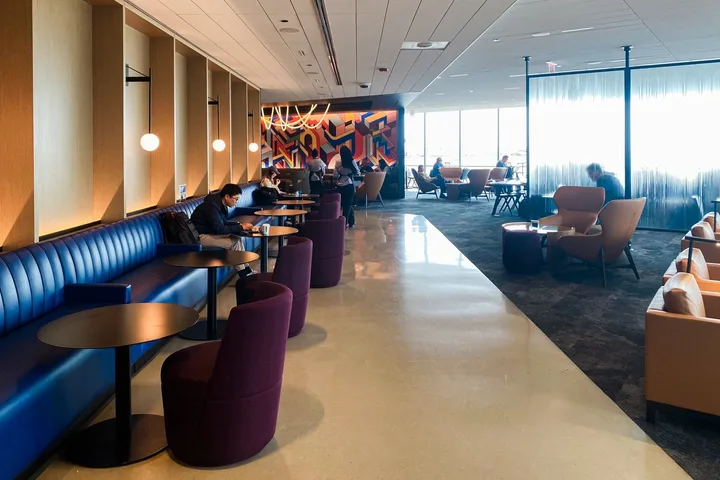 Stylish airline lounge interior with blue booths, purple chairs, and travelers working.