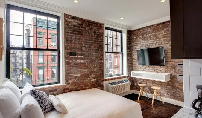 Cozy hotel room with exposed brick walls, large windows, white bedding, and city view.