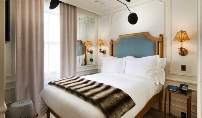 Elegant boutique hotel room with gold-framed headboard, sconce lighting, and luxurious white linens.
