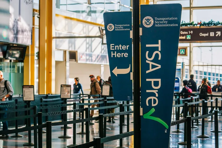 TSA PreCheck lane entrance signs at a busy airport security checkpoint with travelers in background.