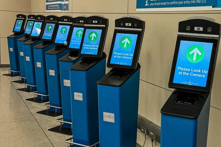A row of Global Entry self-service kiosks with facial recognition screens at a customs hall.