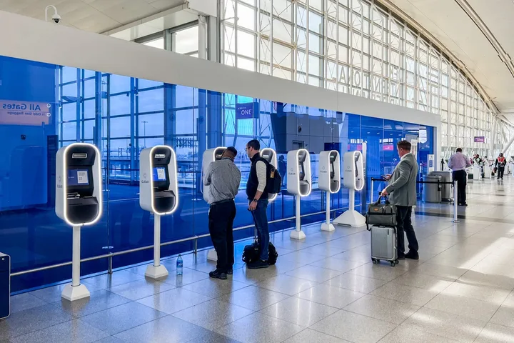 Two travelers using self-service check-in kiosks in a bright, modern airport terminal.