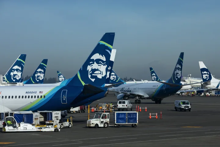 Multiple Alaska Airlines aircraft parked at airport gates with ground crew vehicles.