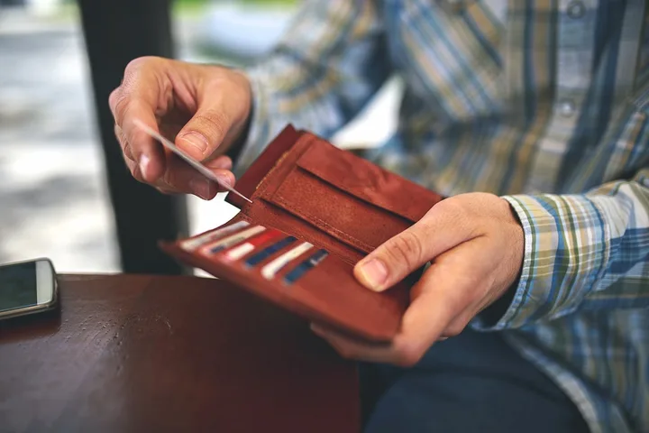 Person pulling a credit card from a brown leather wallet at a table.
