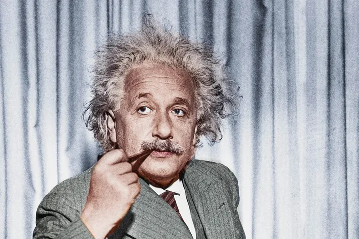 A colorized portrait of Albert Einstein holding a pen, looking thoughtfully at the camera.