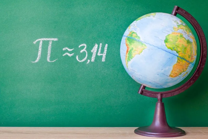 A classroom globe beside a green chalkboard with pi approximately 3.14 written in chalk.