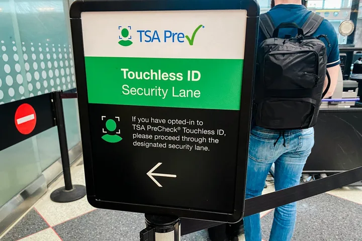 TSA PreCheck Touchless ID Security Lane sign with a traveler holding a backpack in an airport.