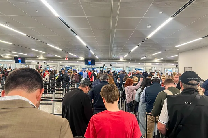 Large crowd of travelers packed into a busy airport security checkpoint with long queues.