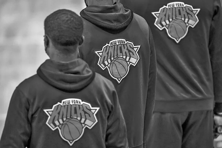 Three people wearing New York Knicks hooded sweatshirts showing the team logo on the back, black and white photo.