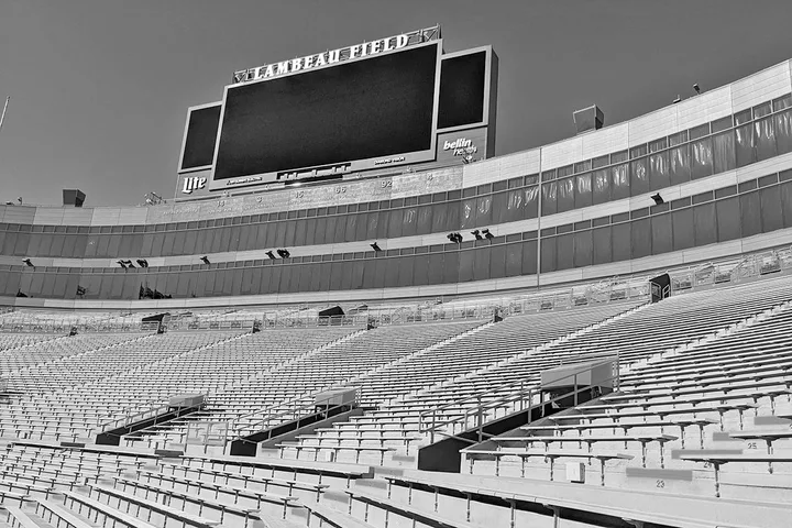 Empty Lambeau Field stadium interior with large scoreboard visible, black and white photo.