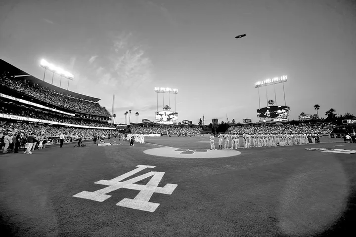 Wide-angle view of Dodger Stadium at dusk with teams lined up on field and LA logo on grass.