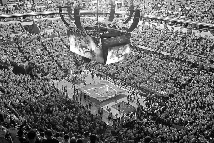 Packed indoor arena aerial view showing a basketball court with team logo during a pre-game ceremony.