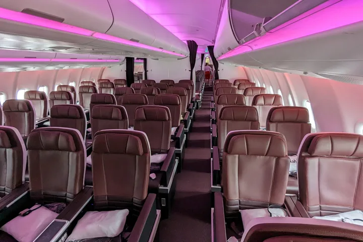 Empty Virgin Atlantic cabin interior with purple mood lighting and rows of leather seats.