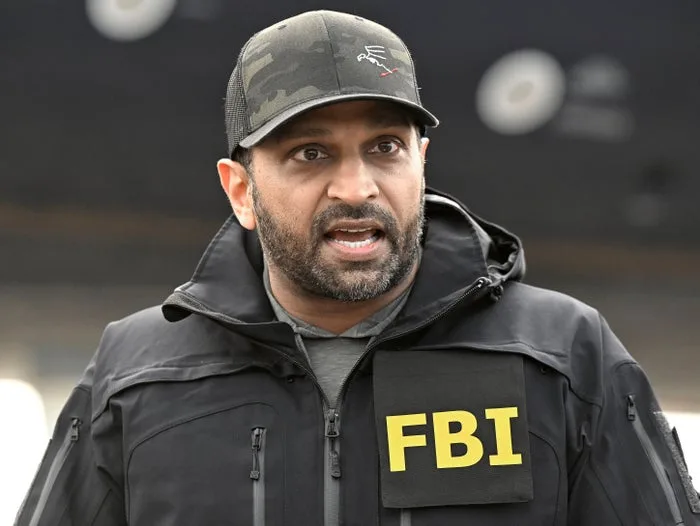 Man wearing an FBI jacket and tactical cap speaking outdoors at an event.