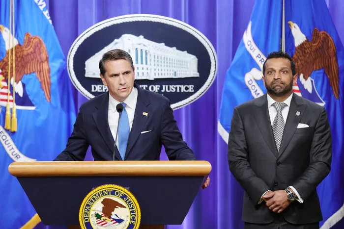 Two men in suits at a Department of Justice press conference podium.