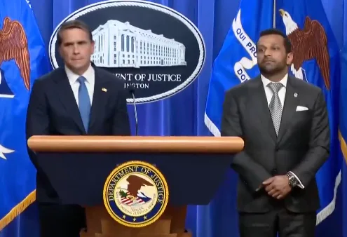 Two men in suits standing at a Department of Justice press conference podium.