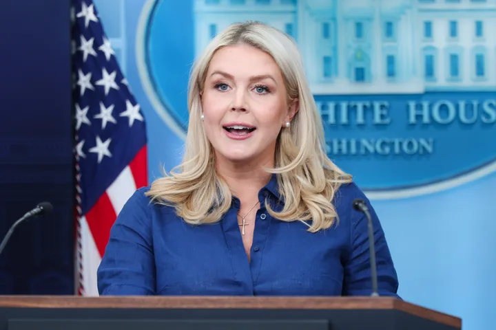 Blonde woman in blue shirt speaking at White House briefing room podium with White House seal behind her.