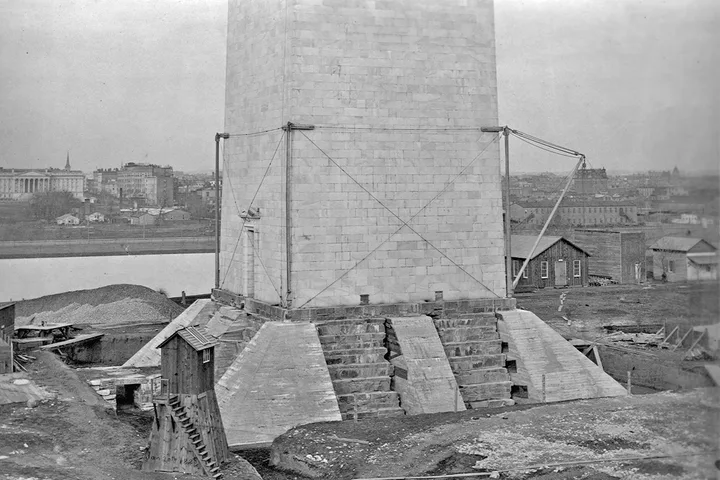 Historic black-and-white photo showing base of Washington Monument under construction with scaffolding and building mate