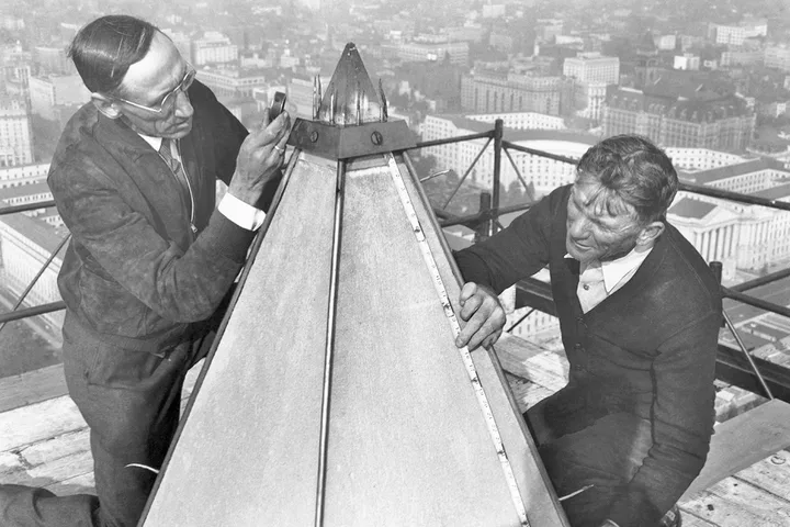 Historic black-and-white photo of two workers examining the aluminum apex cap atop the Washington Monument.