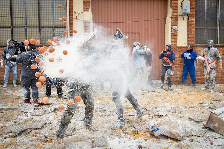 Chaotic outdoor egg and flour throwing festival with participants covered in white powder.