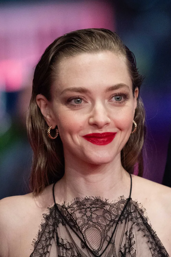 Woman with red lipstick and slicked-back hair in a black lace dress at a formal event.