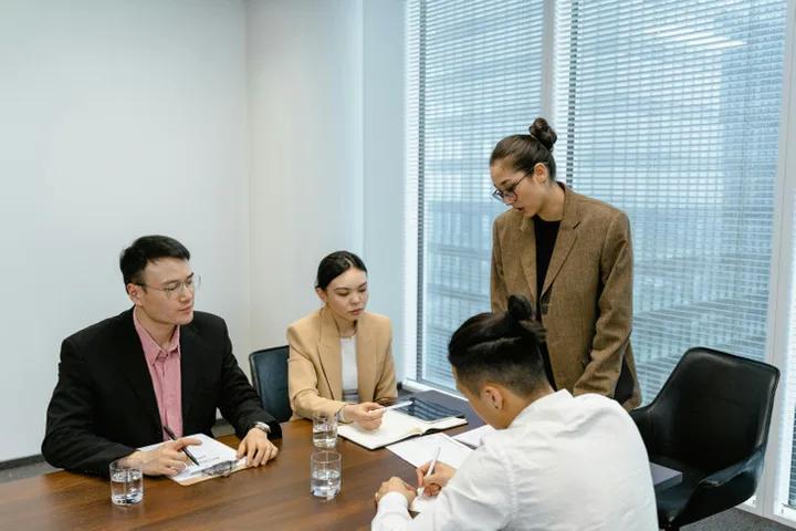 Three professionals in a tense meeting around a conference table in a bright office.