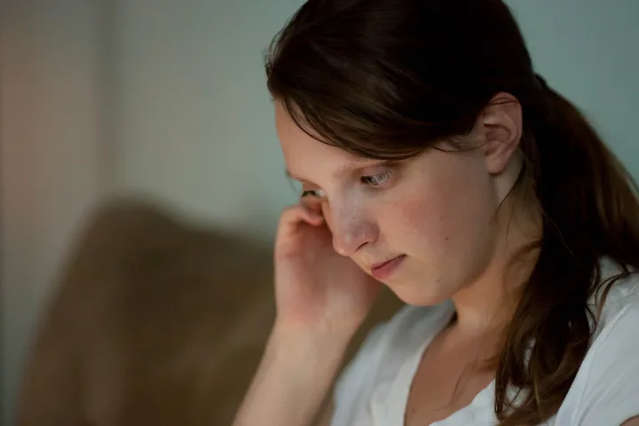 Young woman with dark hair looking down pensively, appearing sad or lost in thought.