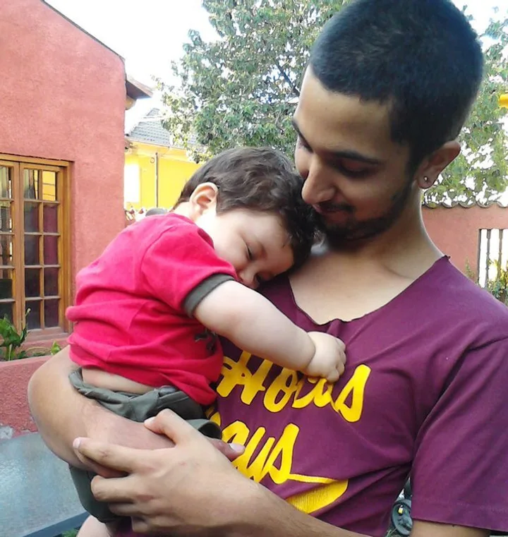 Young man tenderly cradling a sleeping infant against his chest outdoors, warm and intimate moment.