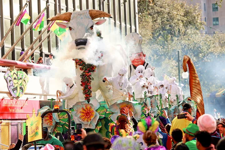 A large elaborate Mardi Gras parade float featuring a giant bull head with smoke effects and white-costumed performers.