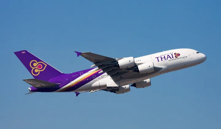 Thai Airways A380 aircraft in purple and white livery flying against a clear blue sky.