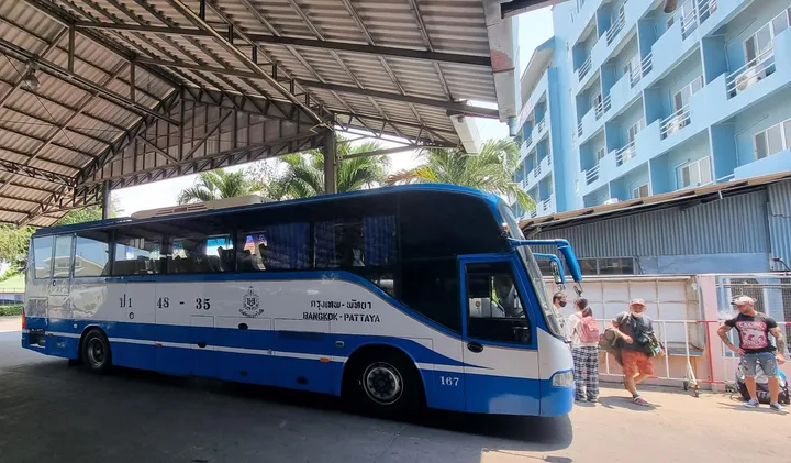 Blue-and-white Bangkok-Pattaya bus parked at a terminal with passengers boarding nearby.