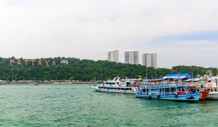 Colorful ferryboats docked at Pattaya City waterfront with the Pattaya City sign visible on a hillside.