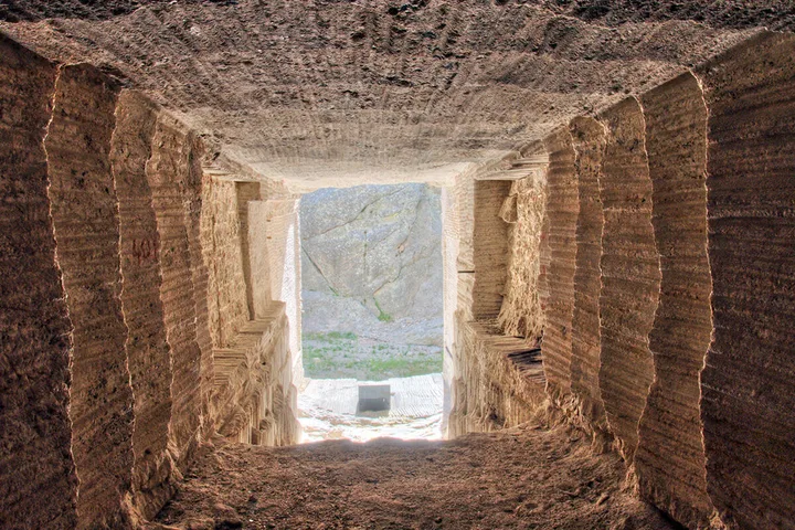 Interior view of an ancient stone chamber or tomb passage with rough carved walls and light at the end.