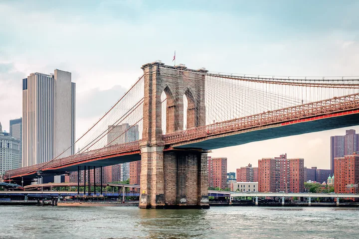 Classic daytime photo of Brooklyn Bridge's stone tower and cables over the East River.