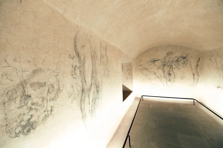 Dimly lit secret underground room with charcoal sketches of faces covering the vaulted walls.