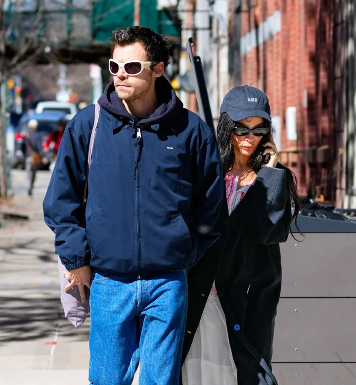 A man and woman walking together on a city sidewalk wearing sunglasses and casual streetwear.