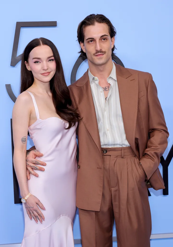 A young couple posing together at a formal event, woman in pink slip dress, man in brown suit.