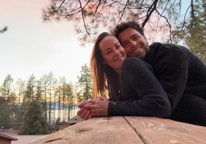A couple leaning together and smiling at sunset outdoors near pine trees, very intimate and romantic.