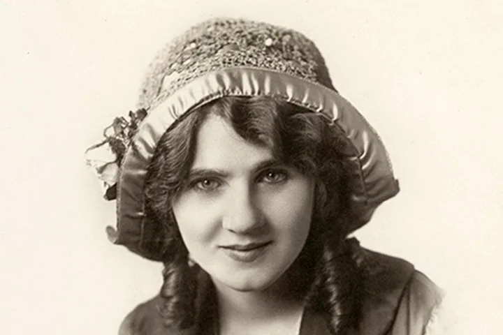 Sepia-toned vintage portrait of a young woman wearing an ornate satin and lace hat.