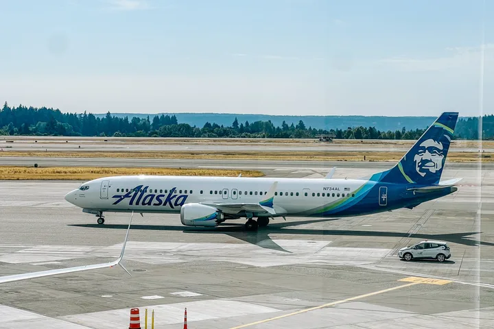 Alaska Airlines Boeing 737 taxiing on airport tarmac on a sunny day.