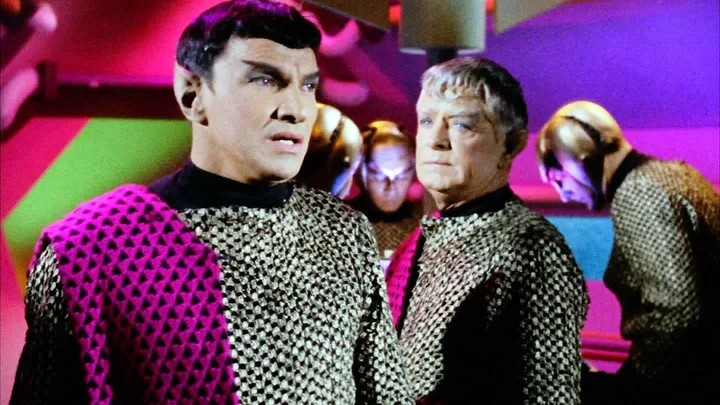 Two actors in classic Star Trek Original Series Romulan costumes on a colorful set.