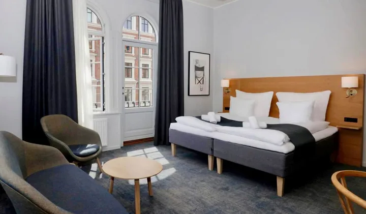 Bright Scandinavian-style hotel room with double bed, arched windows, and modern minimalist furnishings.