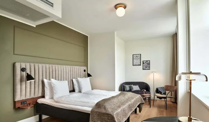 Stylish hotel room with olive green accent wall, upholstered headboard, and Scandinavian design furniture.