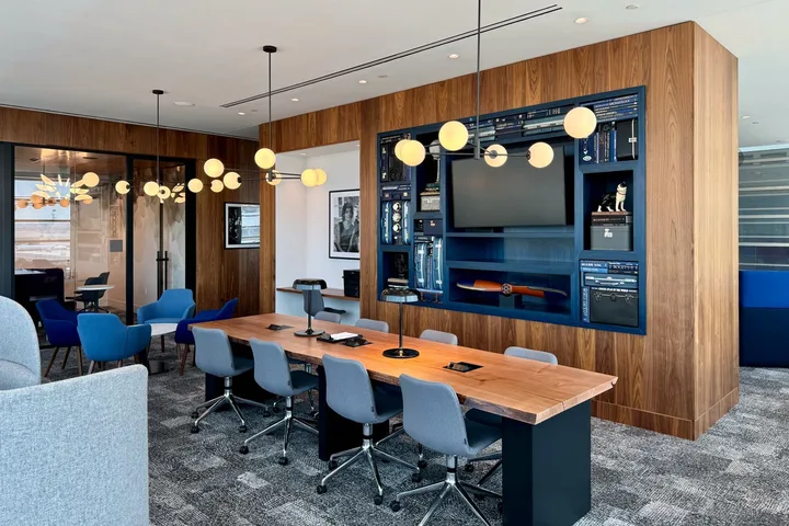 Upscale lounge conference room with long wooden table, blue chairs, and stylish shelving.