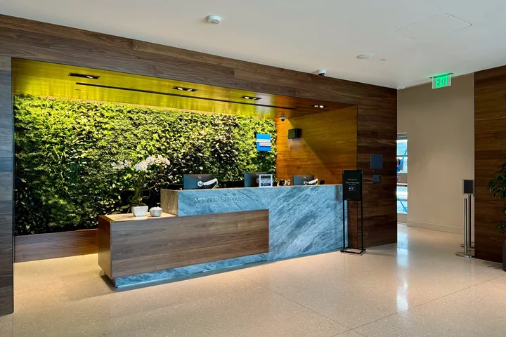 Centurion Lounge member services reception desk with a lush green living plant wall backdrop.